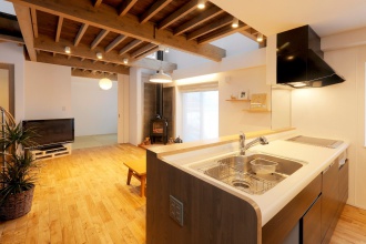 オープンキッチン。腰壁と収納を造作。ブロック構造を残して白く塗装し、間接照明をプラス。1階天を兼ねた2階床にはツーバイ材を使用。株式会社アルティザン建築工房